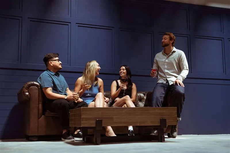 Four friends socializing with cocktails against a navy paneled wall at BLVD Grille